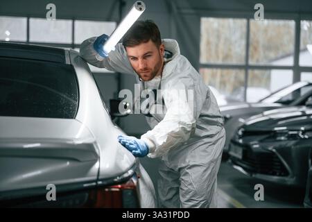 Partie arrière d'automobile. Le garagiste tient l'éclairage et vérifie la surface de la voiture. Banque D'Images