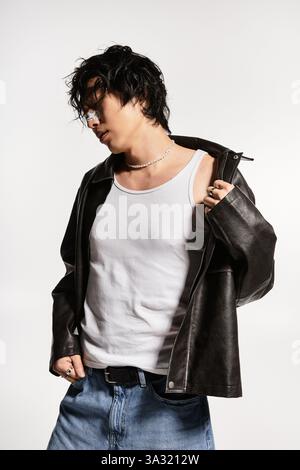 Homme asiatique en veste en cuir et jeans frappe une pose cool dans un studio. Banque D'Images