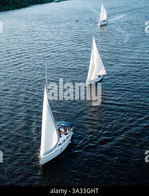 Vue aérienne de trois yachts naviguant sur une rivière par un après-midi ensoleillé. Voiliers blancs sur la rivière - drone vue d'en haut. Banque D'Images