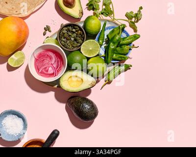 Vue de dessus d'une scène vibrante de préparation de taco sur un fond rose. Ingrédients comme des avocats, des citrons verts, une mangue, des piments verts, des graines de citrouille, oignons rouges Banque D'Images