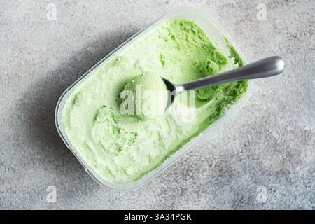 Une vue rapprochée de crème glacée crémeuse à la pistache maison dans un récipient en plastique avec une cuillère en argent. La texture vibrante et la nuance pastel créent une tentation Banque D'Images
