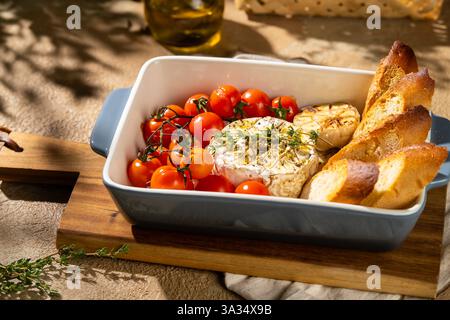 Un plat de camembert cuit au four, accompagné de tomates cerises rôties, d'ail et de tranches de baguette croustillantes dans un plat en céramique. Profitez des saveurs et de la texture Banque D'Images