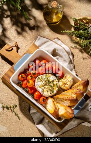 Un délicieux camembert cuit au four servi avec des tomates cerises et du pain croustillant dans un plat vintage. Le thym frais et l'ail rôti ajoutent un charme rustique Banque D'Images