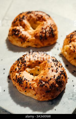 Bagels dorés fraîchement cuits recouverts de graines de sésame. Placés sur une surface en marbre clair, ils créent une scène délicieuse et accueillante pour le petit déjeuner. Banque D'Images