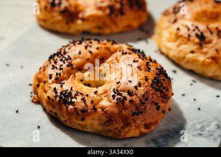 Gros plan de bagels fraîchement cuits recouverts de graines de sésame noir, reposant sur du papier parchemin. La croûte dorée met en valeur leur délicieuse texture Banque D'Images