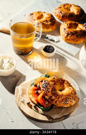 Délicieux bagels fraîchement cuits garni de tomates, câpres et légumes verts. Servi avec un verre de thé vert chaud, l'installation offre une ambiance chaleureuse de petit déjeuner. Banque D'Images