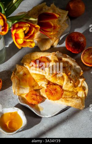 Une délicieuse présentation de crêpes Suzette, avec de fines crêpes drapées dans une riche sauce orange sanguine caramélisée, accompagnée de sang frais oran Banque D'Images