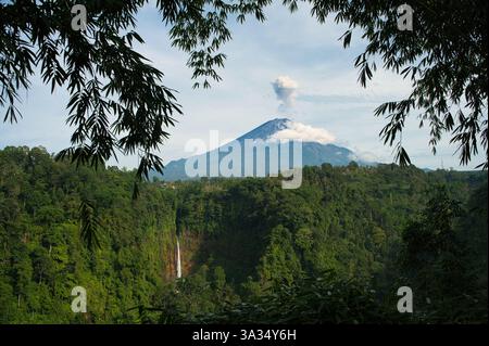 Ce paysage pittoresque capture la cascade de Kaspa Biru pic majestueux entouré de nuages, accompagné d'une cascade en cascade au milieu d'une tropique dense Banque D'Images