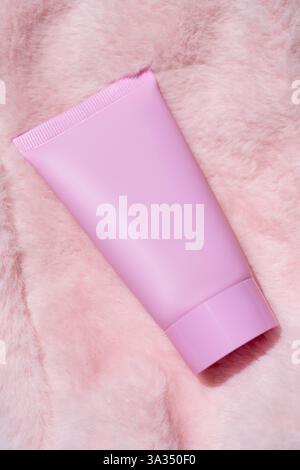 Un tube cosmétique rose repose élégamment sur un fond de fourrure rose doux. Idéal pour les thèmes de soins de la peau et de beauté, mettant en valeur le luxe et la féminité dans le design Banque D'Images