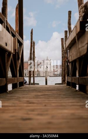 Une vue sereine sur une église vénitienne encadrée par des quais en bois, avec un ciel dégagé au-dessus. La perspective mène l'œil à l'architecture historique, capturi Banque D'Images