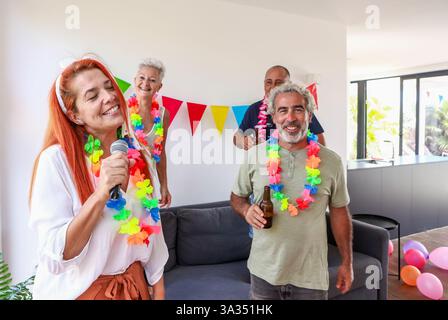 Un groupe de seniors joyeux dans un cadre de fête animé, orné de leis et de drapeaux colorés, profitant de la compagnie de l'autre avec l'un d'eux chantant Banque D'Images
