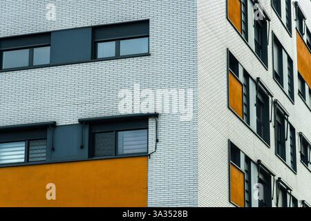 Une façade de bâtiment moderne avec un design distinct ; un mur de briques blanches avec des fenêtres sombres et élégantes et une section orange de sable, apportant une touche de couleur à th Banque D'Images