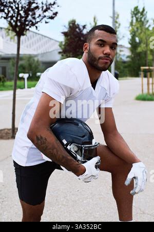 Un joueur de football américain confiant portant un maillot blanc tient un casque à l'extérieur. La scène incarne l'athlétisme, la détermination et l'esprit d'Ameri Banque D'Images