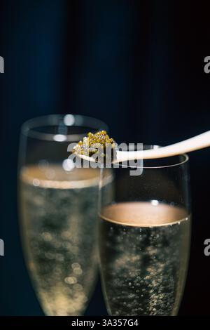 Gros plan capturant du caviar béluga élégamment posé sur une cuillère, juxtaposé au-dessus de deux verres de champagne bouillonnants sur fond sombre Banque D'Images
