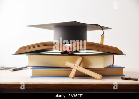 Concept de fond des études et diplômé dans la pile centrale religieuse de livres, avec la Bible ouverte sur le dessus et la table en bois mortarboard avec cros religieux Banque D'Images