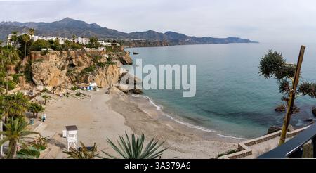 Vue panoramique sur la Playa de Burriana de Nerja, mettant en valeur sa plage de sable, ses falaises escarpées et la chaîne de montagnes lointaine. Banque D'Images