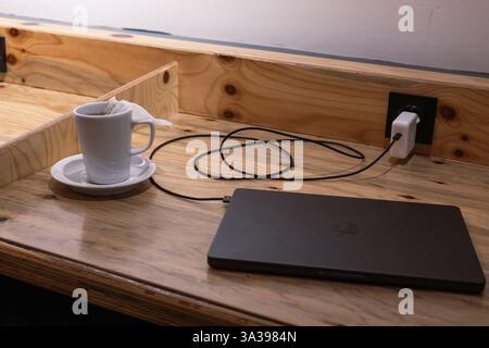 Turkiye, Antalya - 10.03 2025 : table en bois avec MacBook pro, chargeur pour ordinateur portable Apple et tasse de thé dans le centre de coworking, espace. Café pour freelancers, St Banque D'Images