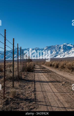 Un chemin de terre le long d'une clôture dans la vallée d'Owens. La Sierra Nevada est couverte de neige en hiver. Banque D'Images