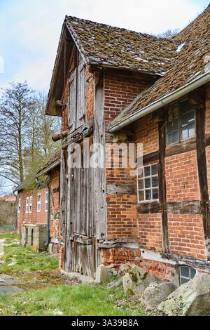 12 mars 2025 - Hoya-Allemagne : ancien moulin à colombages avec un toit couvert de mousse et des portes en bois altérées dans un paysage rural. Banque D'Images