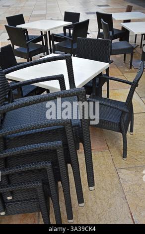 De nombreuses chaises en osier en plastique et quelques tables blanches sont empilées dans la rue près d'un café abandonné Banque D'Images