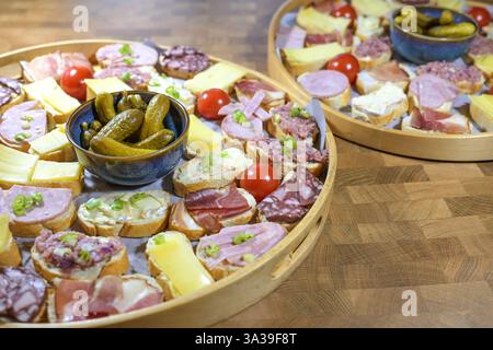 Canapés de fête, petits sandwichs garnis de fromage, de jambon et de saucisses sur un plateau rond avec un bol de cornichons, collation simple avec les doigts, Focus sélectionné, Banque D'Images