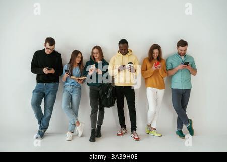 Avec les smartphones à portée de main. Groupe de jeunes se tiennent debout sur fond blanc. Banque D'Images