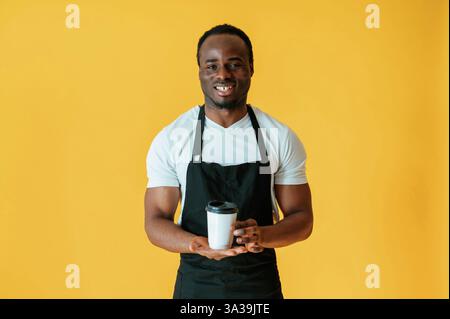 Café dans les mains, ouvrier. Black Man est dans le studio sur fond jaune. Banque D'Images