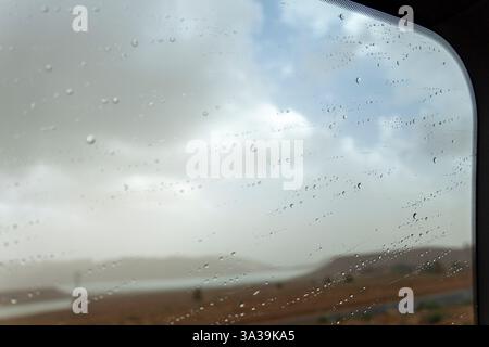 Une vue d'un ciel nuageux à travers une fenêtre couverte de gouttes de pluie Banque D'Images
