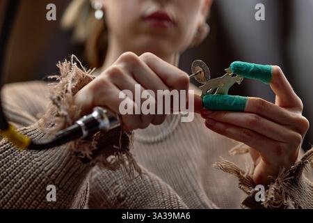 Personne préparant soigneusement la machine de tatouage, leurs mains tenant l'outil enveloppé vert avec l'accent sur l'ajustement détaillé de l'appareil dans un cadre de studio Banque D'Images
