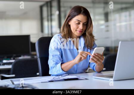Heureux cadre de femme d'affaires mature utilisant le smartphone travaillant dans le bureau. Banque D'Images