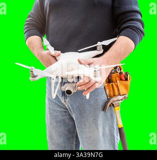 Vue partielle d'un travailleur de la construction portant une ceinture à outils et tenant son drone UAV sur écran vert. Banque D'Images
