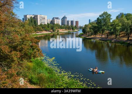 Kyib , Ukraine - 8 septembre 2023 : une journée paisible se déroule alors que les pagayeurs profitent des eaux douces, encadrées par une végétation luxuriante et des bâtiments imposants sous un ciel vibrant. Couple se reposant sur des planches de paddle à la rivière Dnipro Banque D'Images