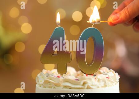 40e anniversaire. Femme allumant le nombre de bougies en forme sur le gâteau contre les lumières floues, gros plan. Effet bokeh Banque D'Images
