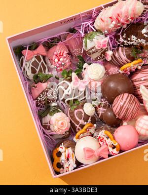 Boîte cadeau rose exquise débordant de fraises enrobées de chocolat magnifiquement décorées et de chocolats gastronomiques assortis Banque D'Images