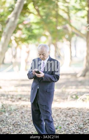 Un parc sur une agréable journée de printemps avec beaucoup de verdure au Japon. Un Japonais à la fin des années 70 portant un costume se lève. Il regarde vers le bas et l'opéra Banque D'Images