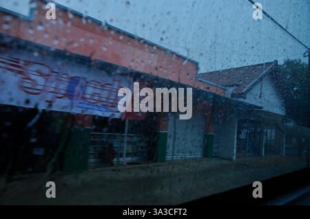 Vue à travers Une fenêtre pluvieuse dans un village tropical avec des maisons et des boutiques Banque D'Images