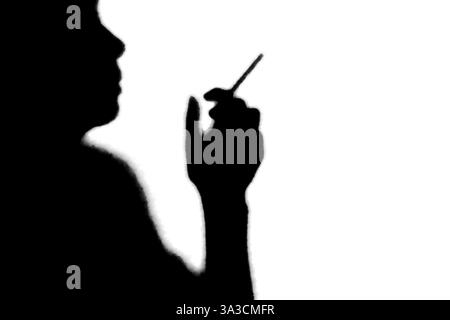 Image d'ombre, silhouette noire et blanche d'une personne avec une cigarette en monochrome Banque D'Images