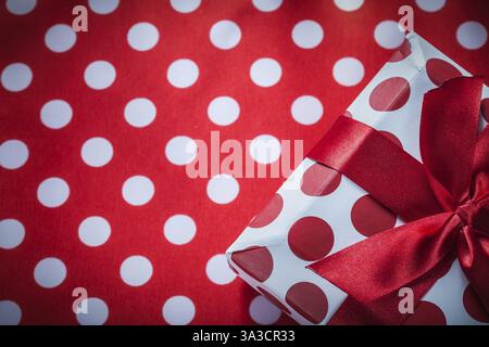 Boîte cadeau enveloppée avec arc sur le concept de vacances de tissu de table rouge à pois Banque D'Images