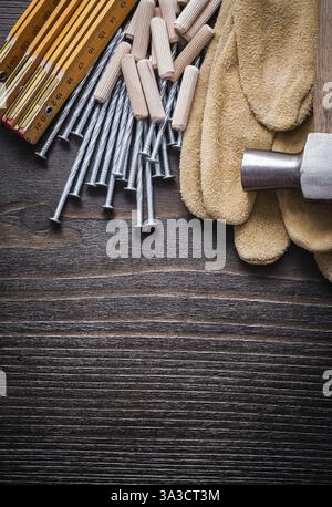 Mètre en bois tas de chevilles griffe marteau gants de protection bruns et clous en métal sur le concept de construction de vue de dessus de planche de bois vintage Banque D'Images