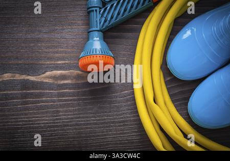 Tuyau en caoutchouc torsadé avec buse de pulvérisation et bottes en gomme sur concept de jardinage en planche en bois vintage Banque D'Images