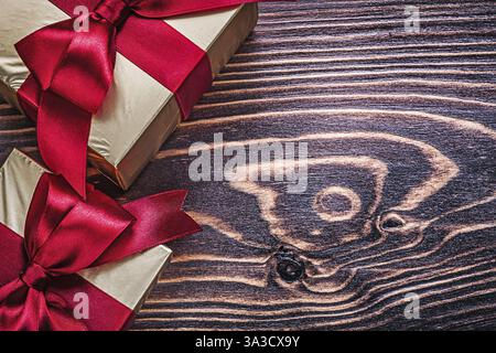 Boîtes cadeaux emballées avec des rubans de satin rouge sur planche de bois Banque D'Images