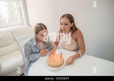 Cake Candles anniversaire : deux femmes soufflent des bougies sur un gâteau d'anniversaire à l'intérieur, célébrant un moment joyeux. Banque D'Images