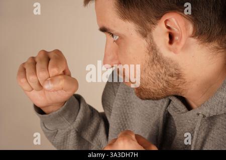 Un homme dans un sweat à capuche sportif se tient debout avec les poings serrés dans une posture de boxe. Sa posture suggère la disponibilité et la détermination. L'image transmet un fort Banque D'Images
