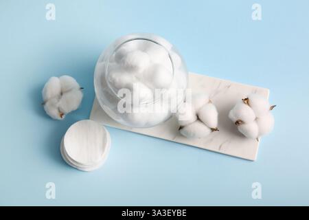 Verre avec des boules de coton, des tampons et des fleurs sur fond bleu Banque D'Images