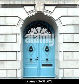 Élégantes portes doubles bleues pastel situées dans une grande entrée en pierre voûtée, ornées de ferronneries complexes. Banque D'Images