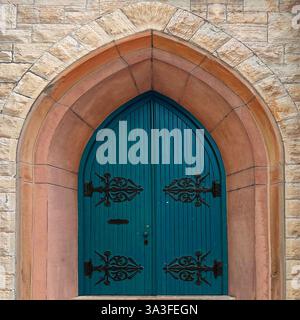 Porte voûtée de style gothique ornée de portes en bois vert foncé agrémentées d'une quincaillerie complexe en fer forgé, située dans une façade historique en pierre. Banque D'Images