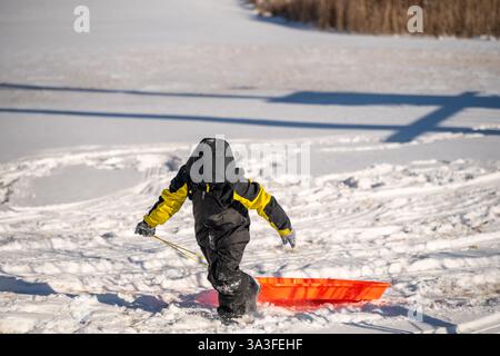 Enfant tirant un traîneau sur une colline enneigée couverte de chenilles Banque D'Images