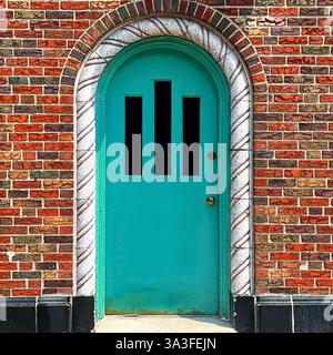 Porte voûtée vert menthe éclatante située dans une façade en briques multicolores, encadrée par une arche décorative en pierre torsadée. Banque D'Images