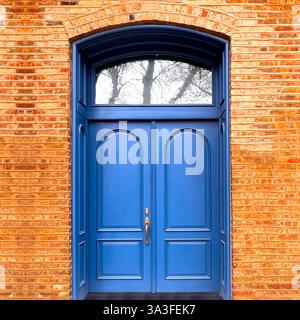 Élégantes portes doubles cintrées bleu foncé placées dans une façade en briques aux tons chauds, avec moulures complexes et une fenêtre arrière classique. Banque D'Images