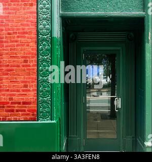 Porte en verre verte placée à l'intérieur., avec des ferronneries florales décoratives, des détails architecturaux vert foncé et une façade en briques rouges. Banque D'Images